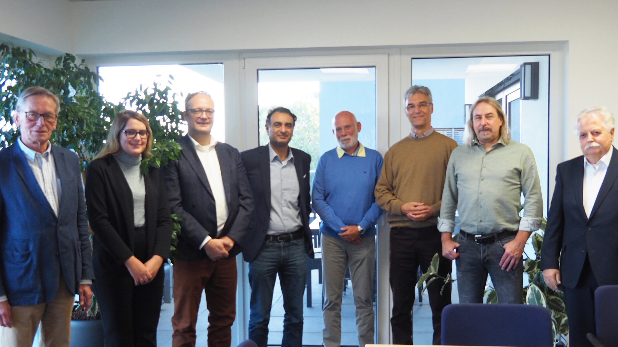 Abbildung acht Personen vor einer Fensterwand