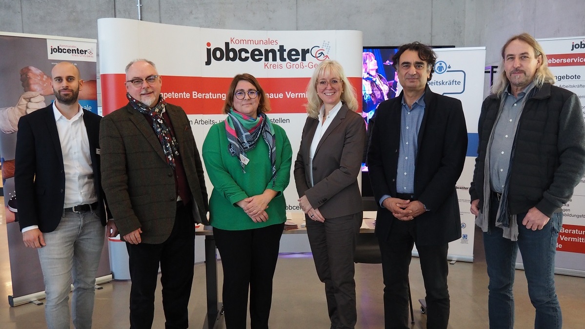 Abbildung sechs Personen vor einer Plakatwand