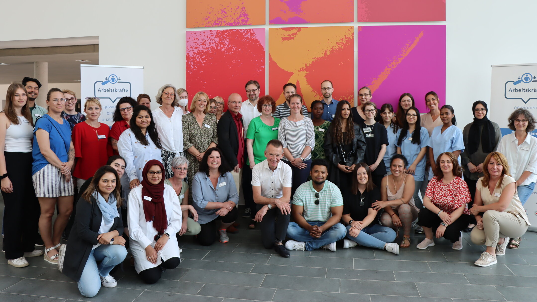 Etwa drei Dutzend Personen stehen und sitzen vor einer Wand